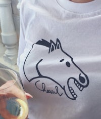 a woman holding a glass of wine and a t - shirt with a horse head on it
